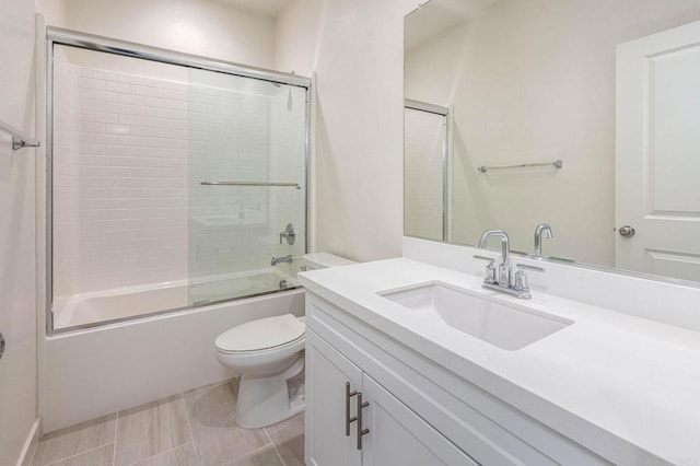 full bath with toilet, vanity, and shower / bath combination with glass door