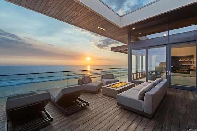 deck at dusk with a beach view, a fire pit, and a water view