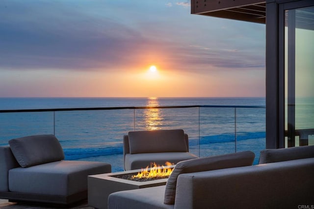 balcony at dusk featuring a fire pit and a water view