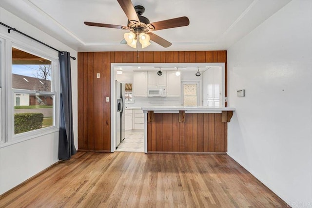 kitchen featuring white microwave, light countertops, a peninsula, light wood-style floors, and white cabinetry