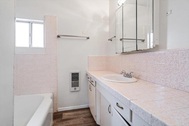 bathroom with a tub to relax in, wood finished floors, decorative backsplash, baseboards, and vanity