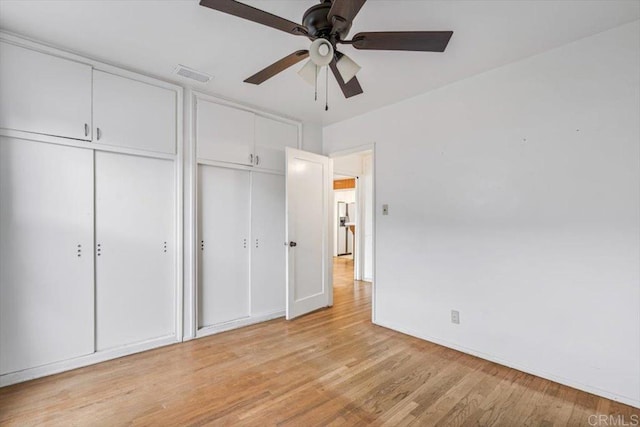 unfurnished bedroom with light wood-type flooring, visible vents, multiple closets, and a ceiling fan