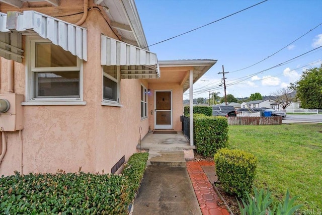 view of exterior entry featuring stucco siding, a yard, and fence