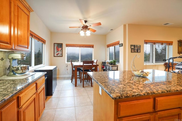 kitchen featuring visible vents, tasteful backsplash, dark stone counters, brown cabinetry, and light tile patterned floors