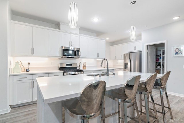 kitchen with light wood finished floors, a sink, appliances with stainless steel finishes, white cabinets, and a kitchen island with sink