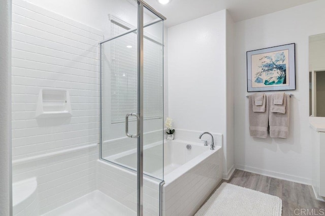 bathroom with a shower stall, a bath, wood finished floors, and baseboards