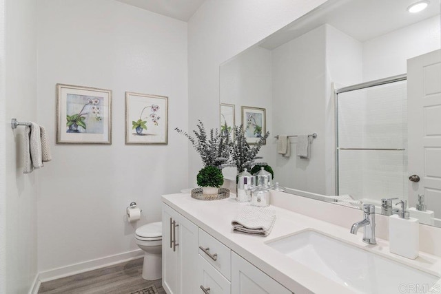 bathroom featuring vanity, wood finished floors, baseboards, tiled shower, and toilet