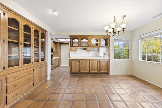 kitchen featuring visible vents, decorative backsplash, light countertops, glass insert cabinets, and a chandelier