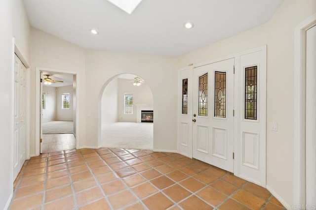 entryway with a glass covered fireplace, light tile patterned floors, recessed lighting, and arched walkways