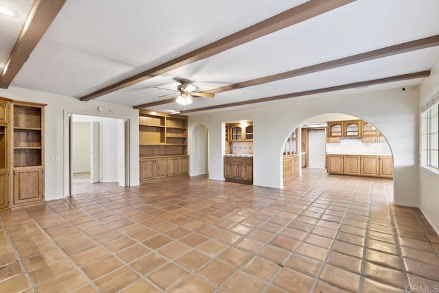 unfurnished living room featuring beam ceiling, a ceiling fan, arched walkways, light tile patterned flooring, and baseboards