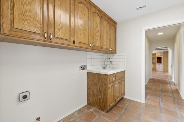 laundry area with visible vents, hookup for an electric dryer, baseboards, cabinet space, and arched walkways