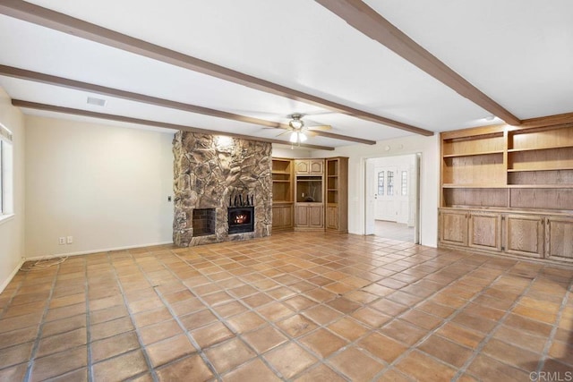 unfurnished living room with tile patterned floors, beam ceiling, built in shelves, a stone fireplace, and ceiling fan