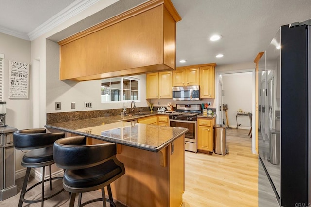 kitchen featuring a breakfast bar, ornamental molding, appliances with stainless steel finishes, a peninsula, and light wood finished floors