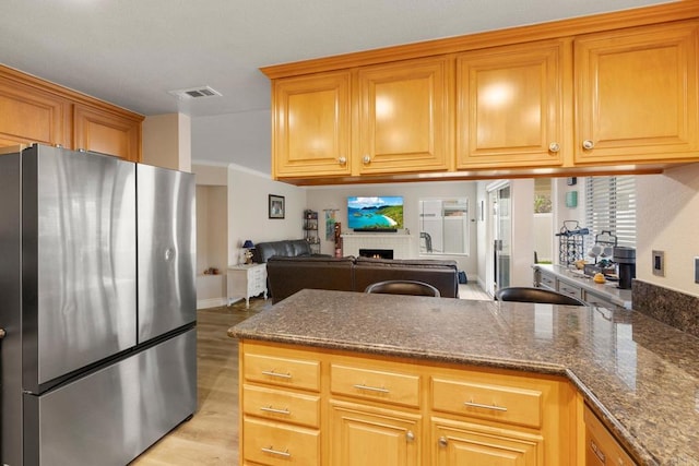 kitchen featuring visible vents, light wood finished floors, dark stone counters, a fireplace, and freestanding refrigerator