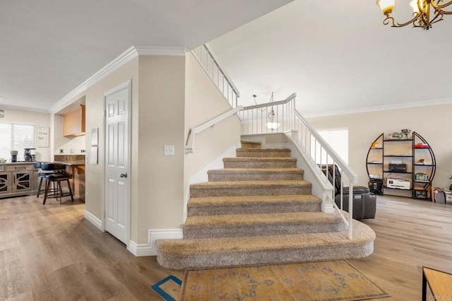 staircase with a chandelier, ornamental molding, baseboards, and wood finished floors