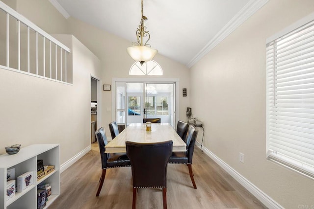 dining space featuring baseboards, crown molding, light wood-style floors, and vaulted ceiling