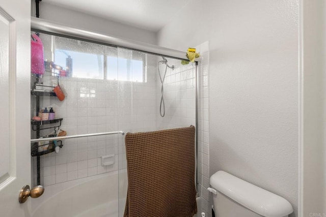 bathroom with toilet, a textured wall, and tiled shower