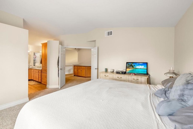 bedroom featuring visible vents, baseboards, lofted ceiling, ensuite bathroom, and light colored carpet