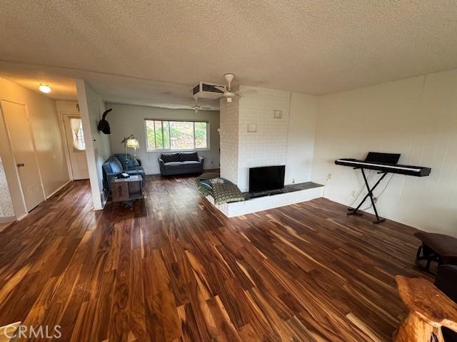 unfurnished living room with a textured ceiling, a brick fireplace, wood finished floors, and a ceiling fan