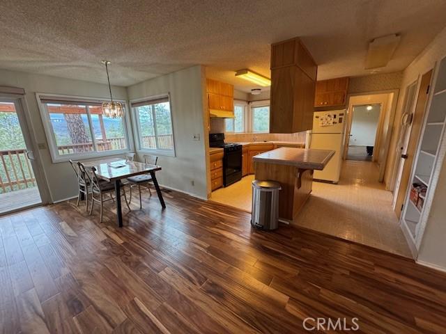 kitchen featuring a textured ceiling, dark wood finished floors, freestanding refrigerator, an inviting chandelier, and black range with gas cooktop