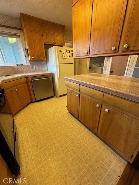 kitchen with light floors, dishwasher, freestanding refrigerator, brown cabinetry, and a textured ceiling