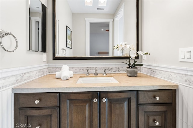 bathroom featuring visible vents, vanity, and a wainscoted wall