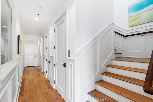 hall featuring recessed lighting, stairway, light wood-style floors, and a decorative wall