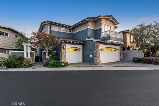 view of front of house featuring concrete driveway, a balcony, a garage, and stone siding