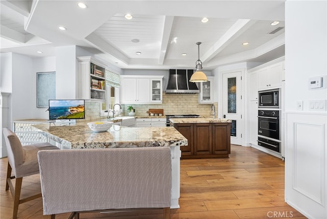 kitchen with light wood finished floors, wall oven, premium range hood, beam ceiling, and a peninsula