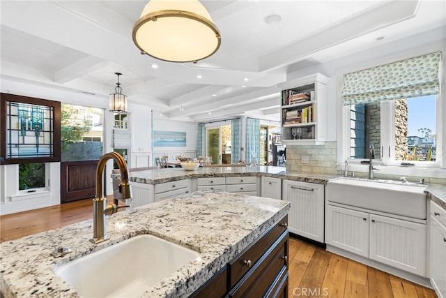 kitchen featuring decorative backsplash, beamed ceiling, light wood-style floors, and a sink