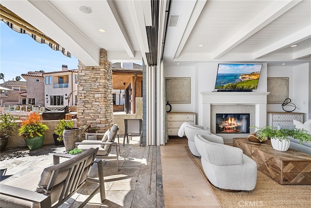 living area featuring visible vents, beam ceiling, wood finished floors, a glass covered fireplace, and recessed lighting