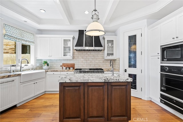 kitchen with custom exhaust hood, oven, built in microwave, and a sink