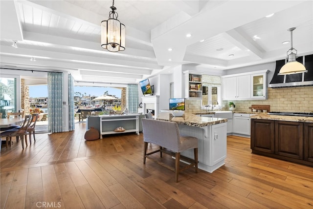 kitchen with light stone counters, beam ceiling, custom exhaust hood, and hardwood / wood-style floors