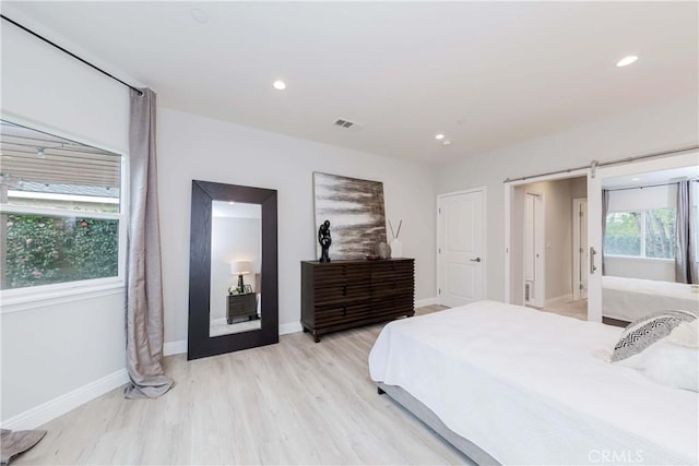 bedroom with recessed lighting, light wood-style flooring, baseboards, and a barn door