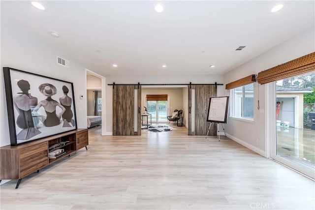 unfurnished living room featuring recessed lighting, a barn door, light wood-style floors, and visible vents