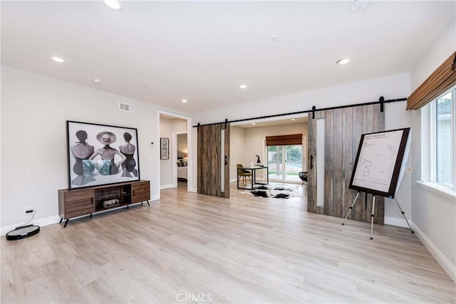 living room with a barn door, baseboards, light wood-style floors, and visible vents