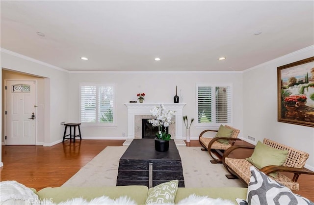 living area featuring a high end fireplace, ornamental molding, baseboards, and wood finished floors