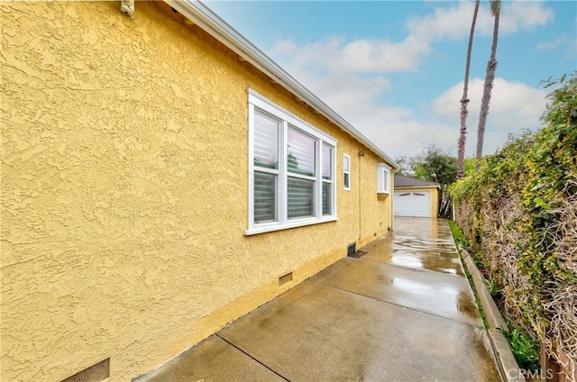 view of side of property with crawl space, an outbuilding, a detached garage, and stucco siding