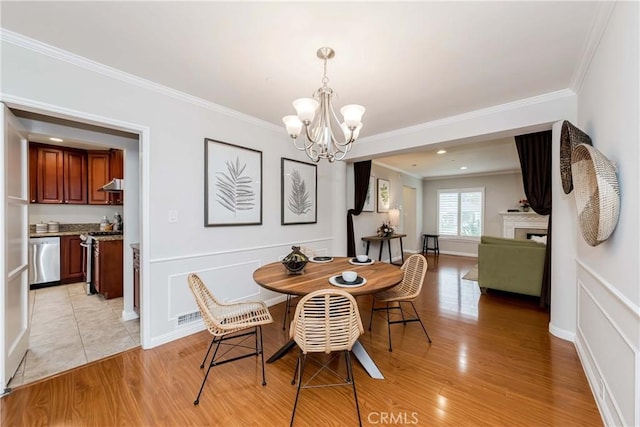 dining area featuring crown molding, light wood-type flooring, a fireplace, a notable chandelier, and a decorative wall