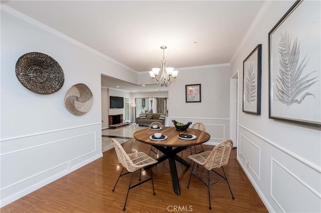 dining area with wood finished floors, a notable chandelier, ornamental molding, and a decorative wall