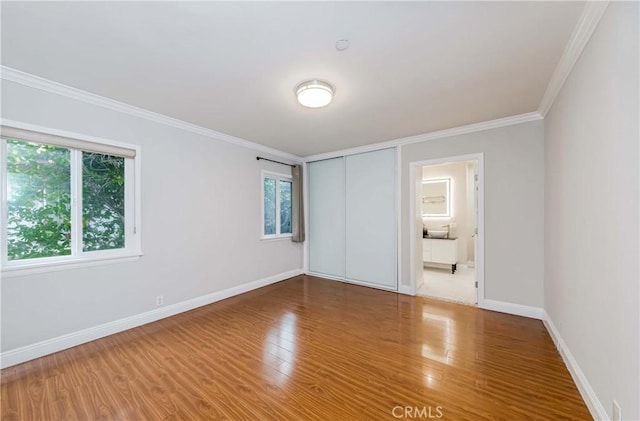 unfurnished bedroom featuring baseboards, multiple windows, wood finished floors, and crown molding