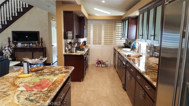 kitchen with a sink, light stone counters, dark brown cabinetry, and built in fridge