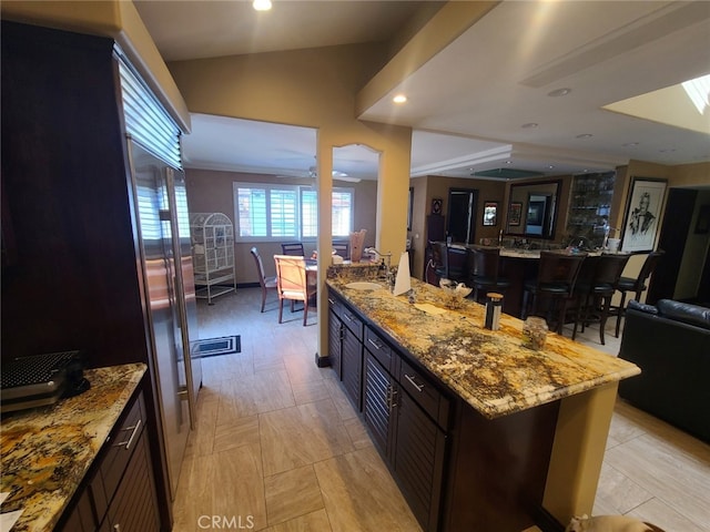 kitchen featuring open floor plan, lofted ceiling, light stone counters, recessed lighting, and a sink