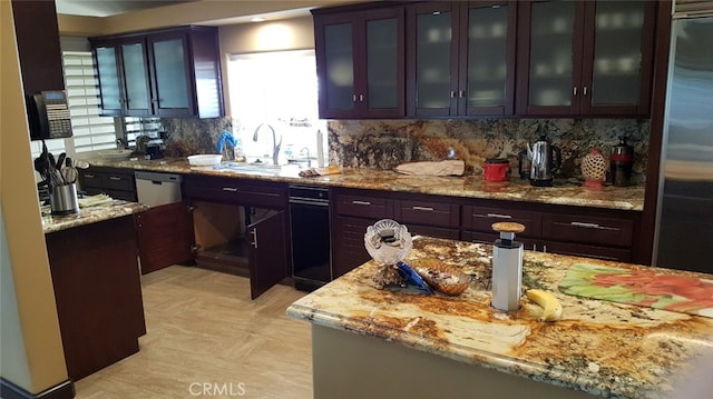 kitchen featuring light stone counters, a sink, glass insert cabinets, high quality fridge, and backsplash