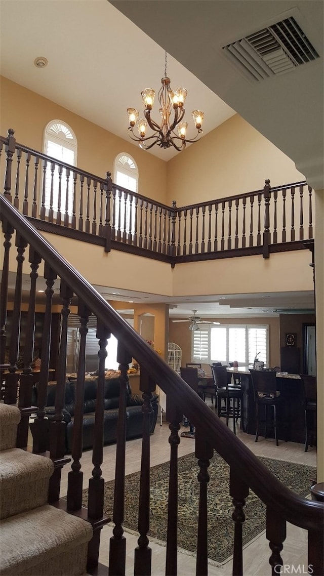 stairway featuring visible vents, a high ceiling, and ceiling fan with notable chandelier