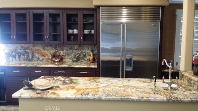 kitchen with a sink, glass insert cabinets, light stone counters, and built in fridge