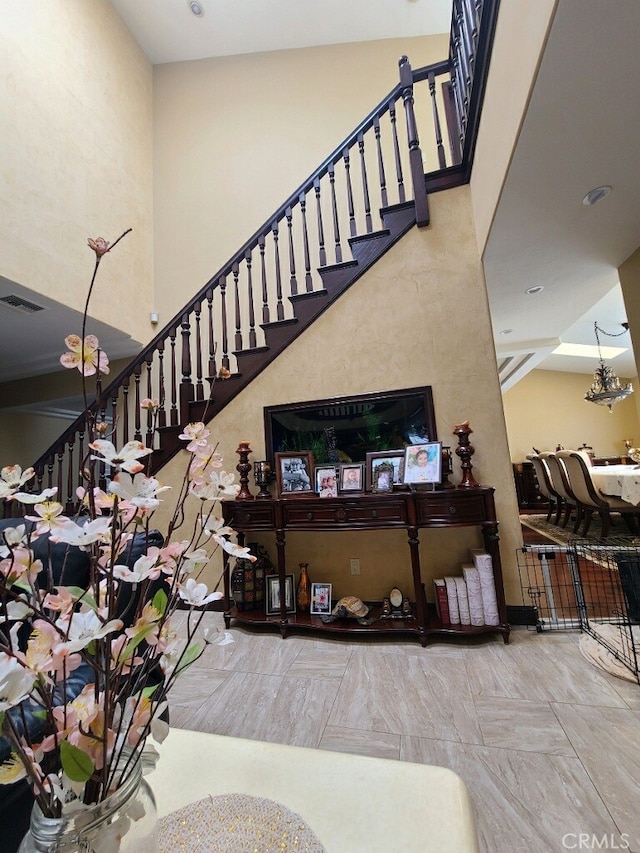 stairs with an inviting chandelier, a high ceiling, and visible vents