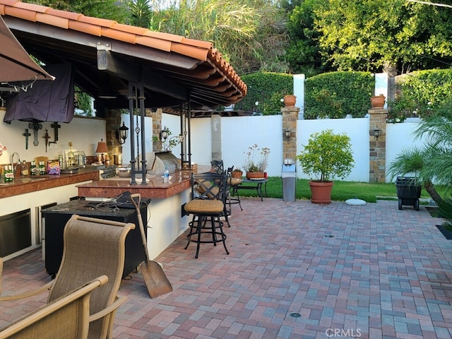 view of patio featuring outdoor wet bar, exterior kitchen, fence, and a sink