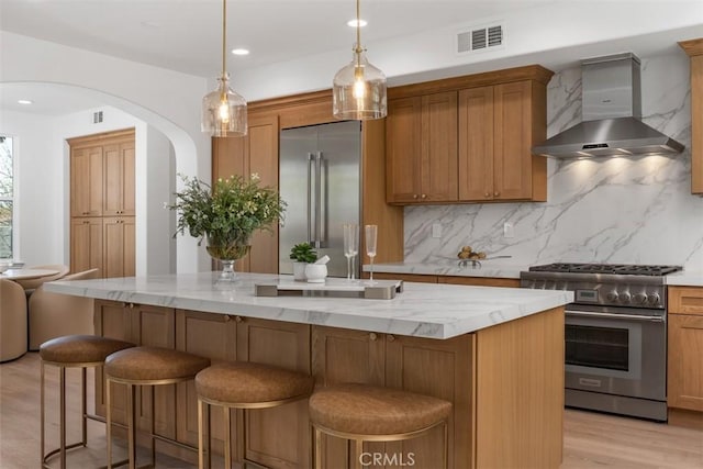 kitchen with a center island, wall chimney range hood, premium appliances, decorative backsplash, and hanging light fixtures