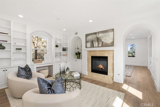 15 Cavaillon, Newport Coast, CA 92657 - living room with light wood-type flooring, built in shelves, a tiled fireplace, recessed lighting, and ornamental molding